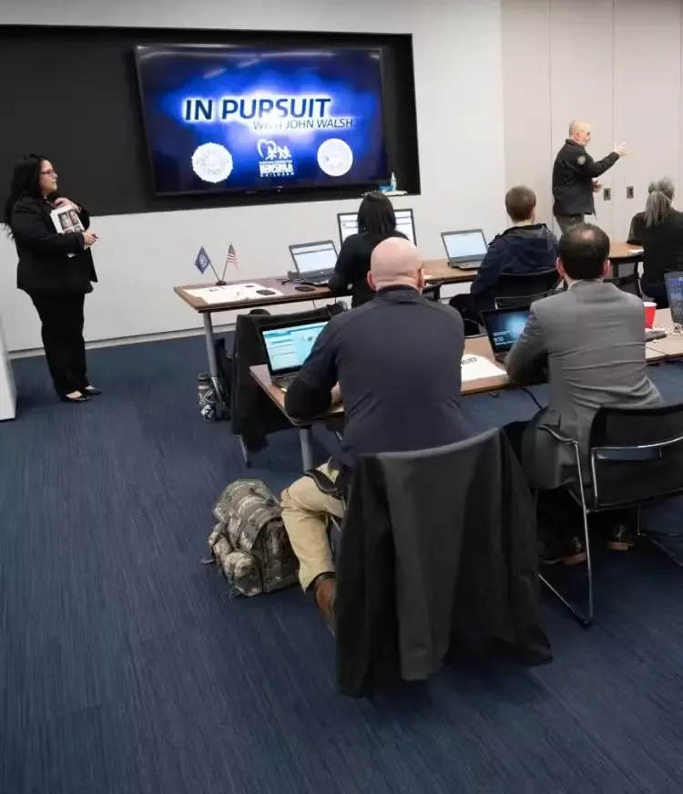 People in a room in front of huge screen for missing people